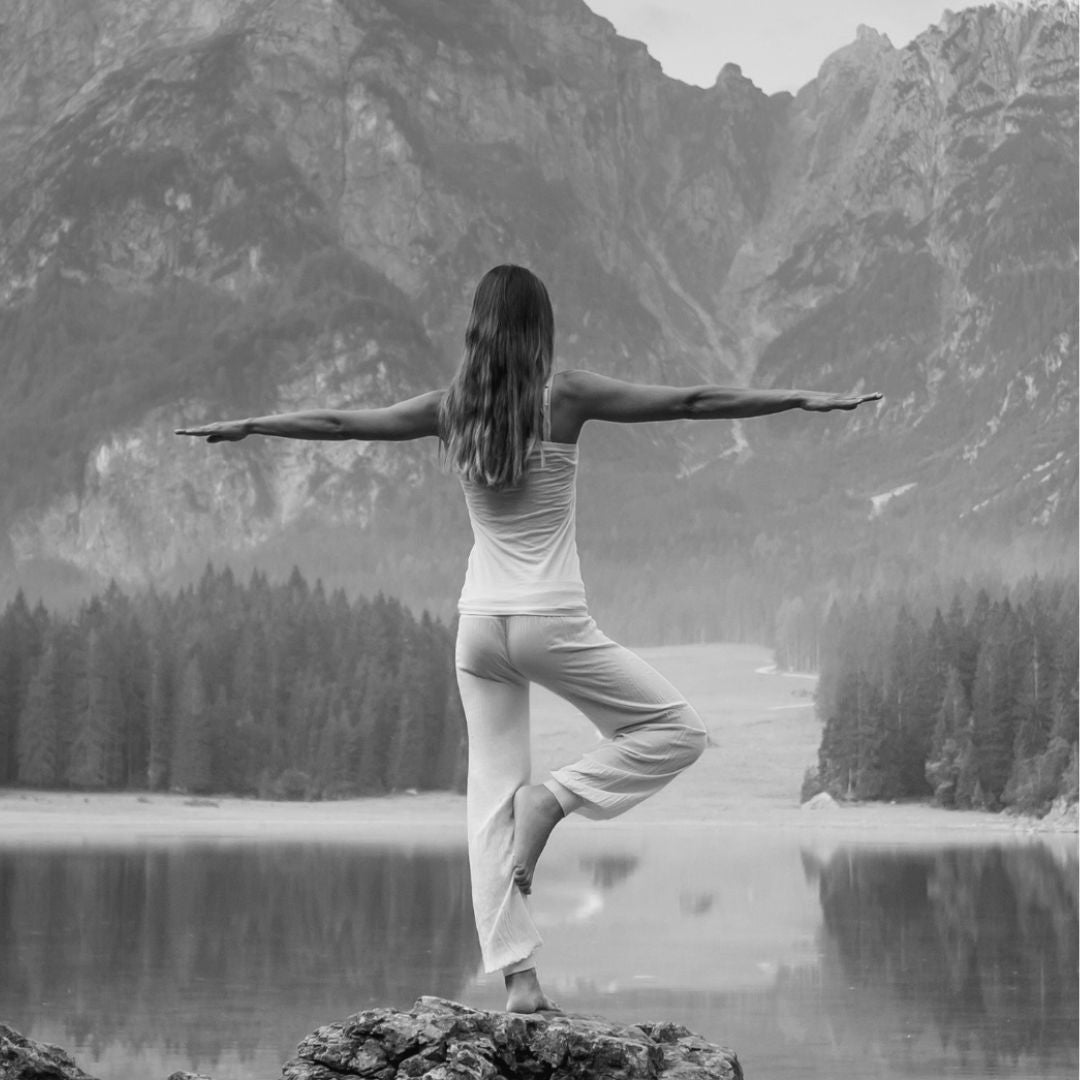 Frau macht Yoga in der Natur am See, umgeben von Bergen – Symbol für Wohlbefinden, Balance und Achtsamkeit