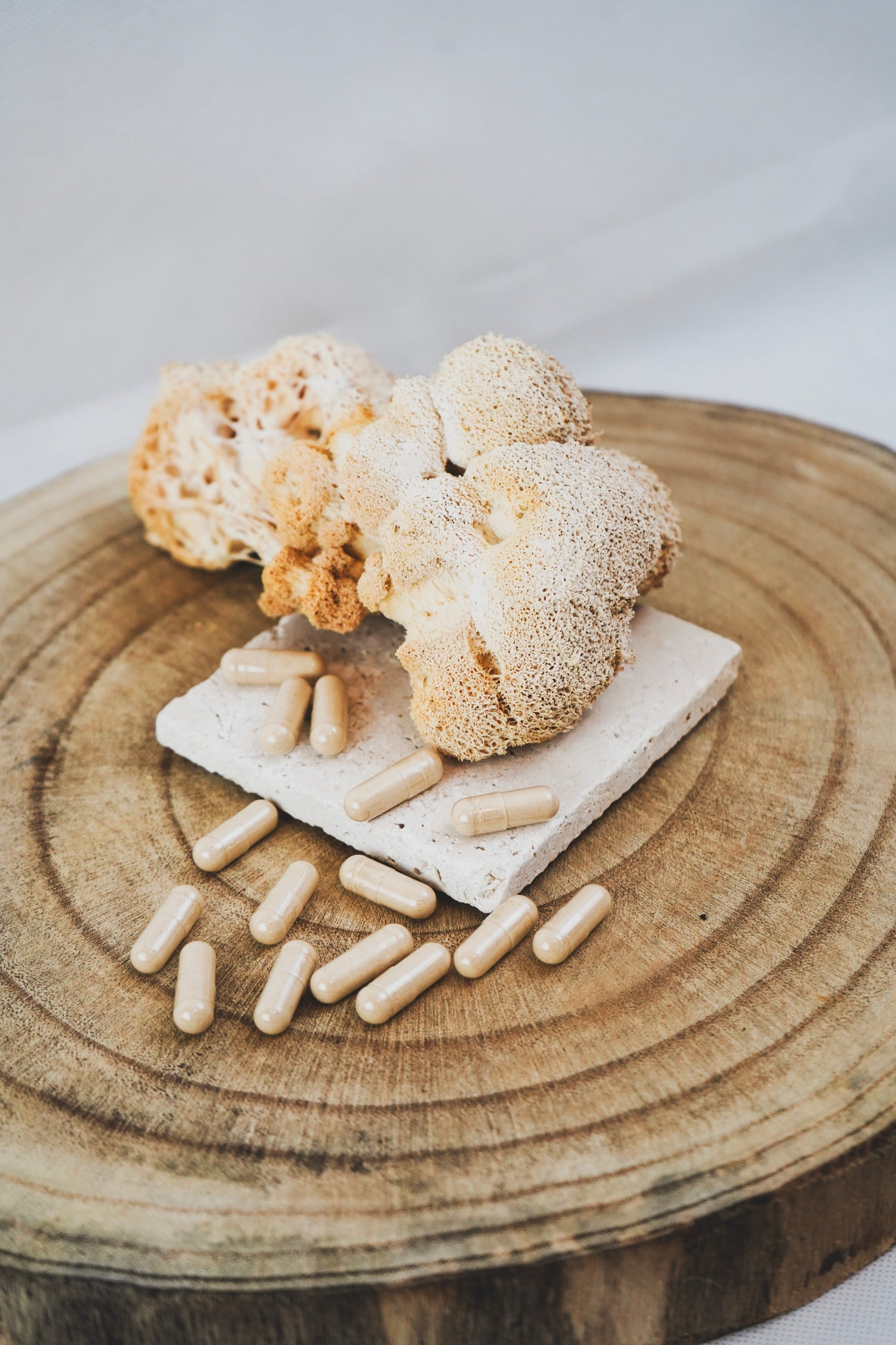 Igelstachelbart-Pilz (Hericium erinaceus) und beige Vitalpilz-Kapseln auf Holzplatte, natürliche Nahrungsergänzung, Produktpräsentation in Nahaufnahme