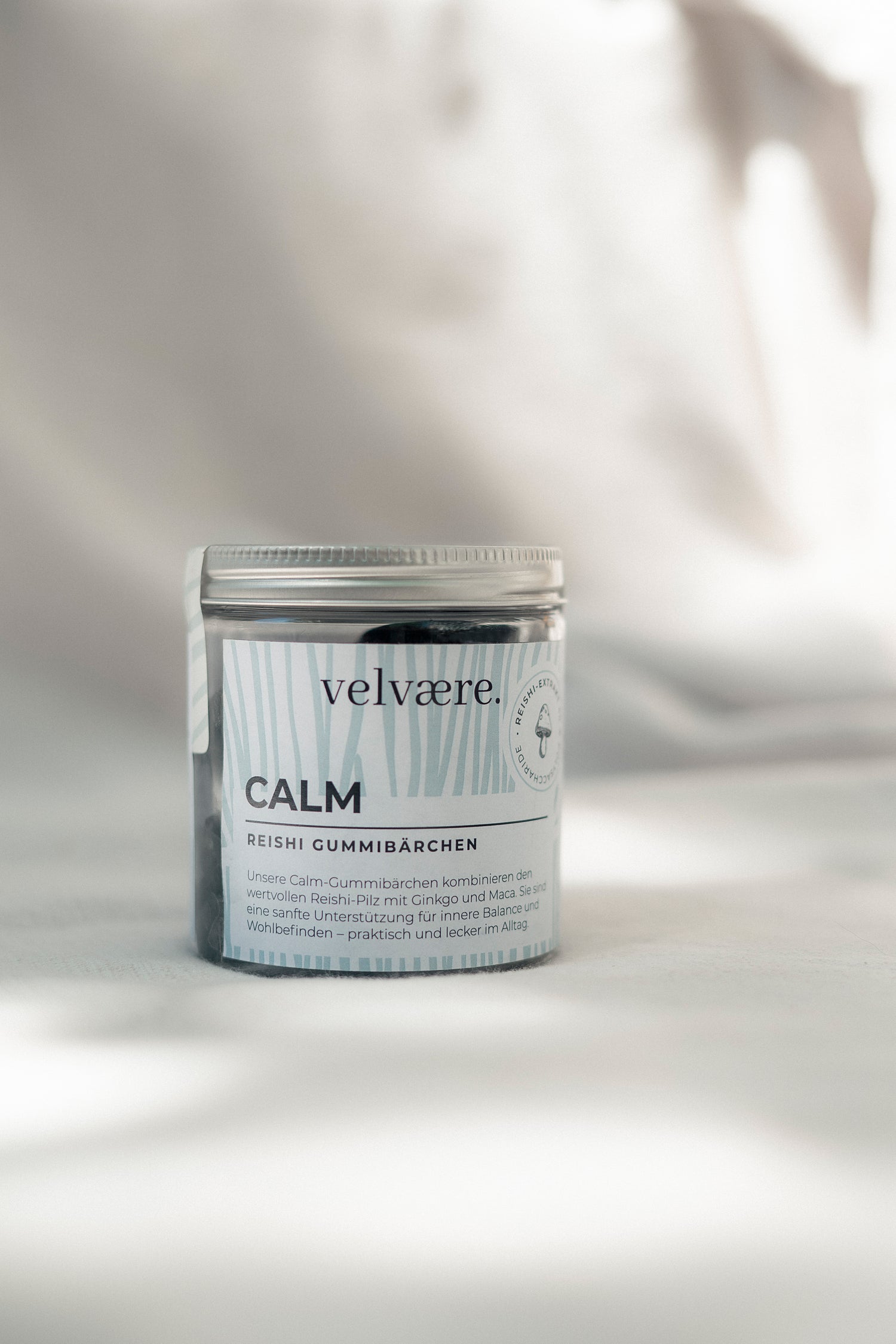 Velvaere CALM Reishi Gummibärchen in einer Glasdose auf hellem Stoffuntergrund. Nahrungsergänzung mit Reishi, Ginkgo und Maca für innere Balance und Wohlbefinden.