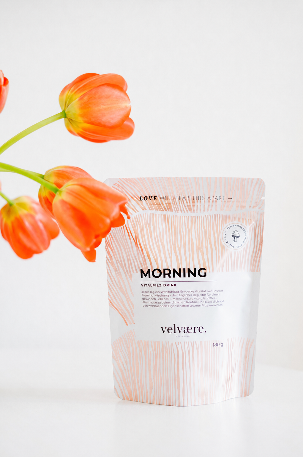 Velvaere MORNING Vitalpilz Drink in einer minimalistischen Produktinszenierung mit leuchtend orangefarbenen Tulpen. Die natürliche Kaffee-Alternative für mehr Energie, Fokus und Wohlbefinden im Alltag.