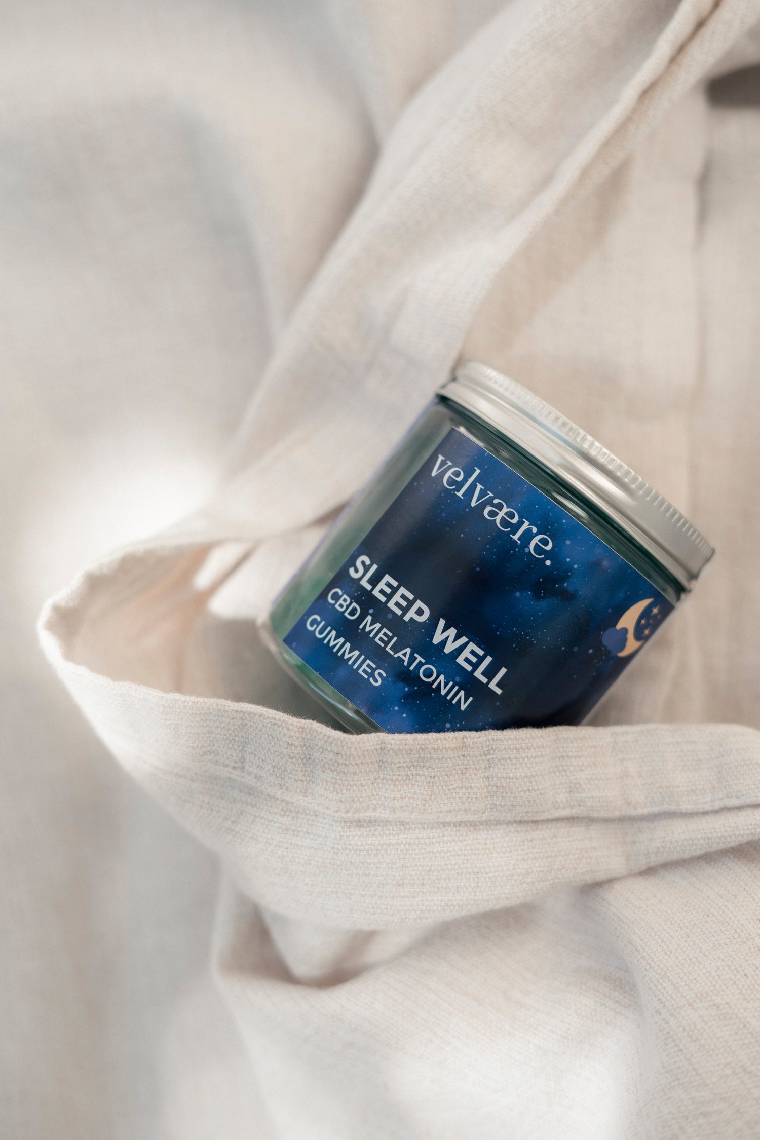 Velvaere SLEEP WELL Gummies mit Melatonin in einer Glasdose auf hellem Stoff. Nahrungsergänzung für die Abendroutine und einen erholsamen Schlaf.